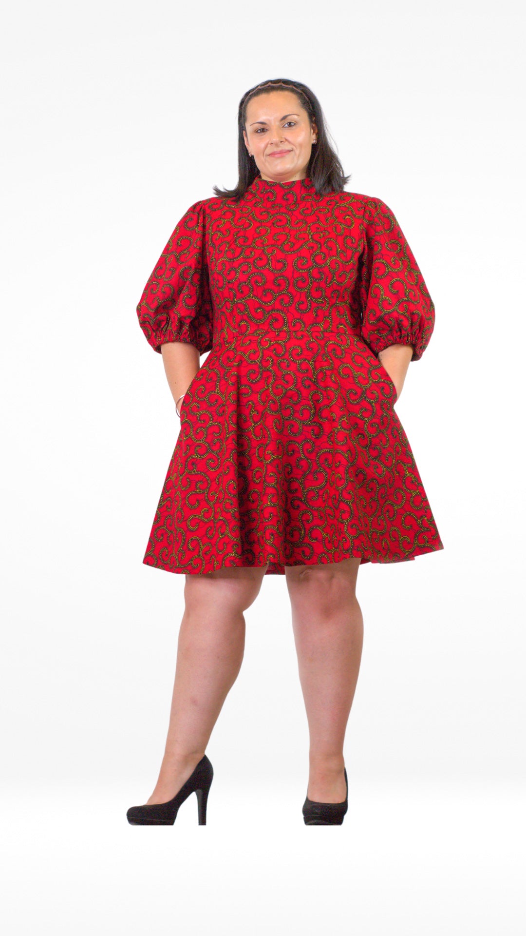 A woman confidently poses with hands in pockets in in a short red print puff-sleeve dress, paired with black heels.