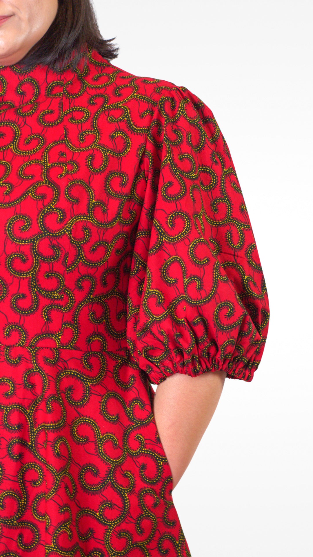 A close-up view highlighting the charming puff sleeve and a practical pocket of the red dress and its swirly gold elements.