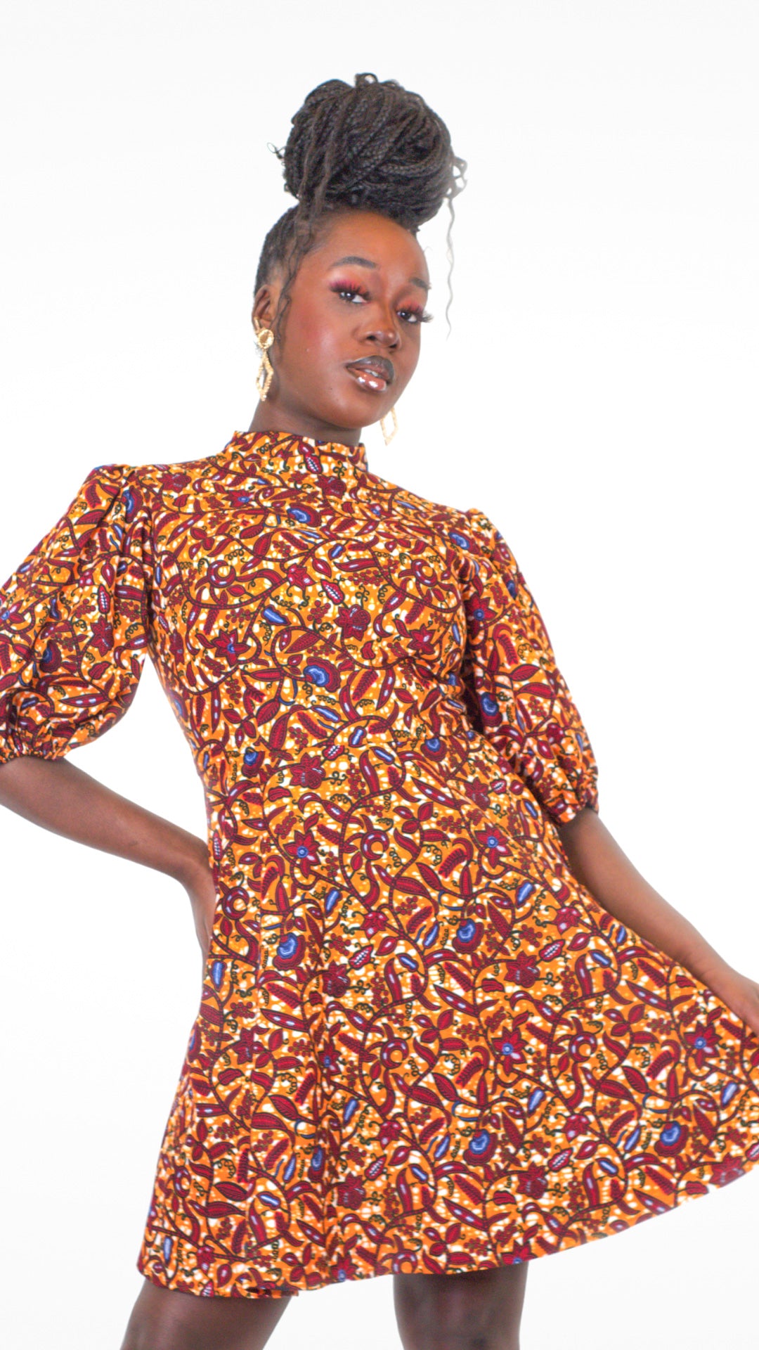 A close up of a model confidently posing in a short orange puff sleeve dress, highlighting the silhouette of the dress and its detailed elements.