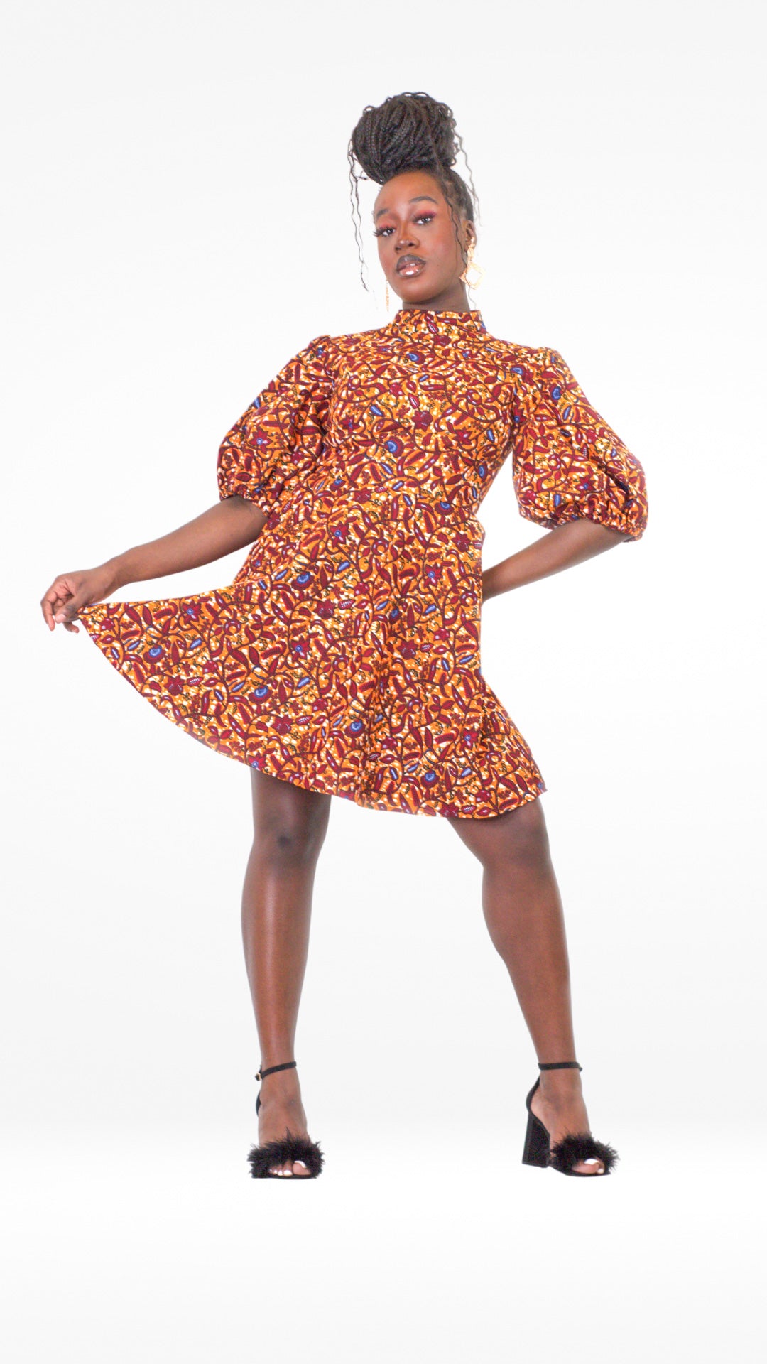 A woman confidently poses in a short orange puff sleeve dress, paired with black fluffy heels.