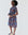 Woman in a knee-length, short-sleeved wrap dress with a geometric African print in blue, gold, and burgundy, styled with a waist tie and wedge heels.