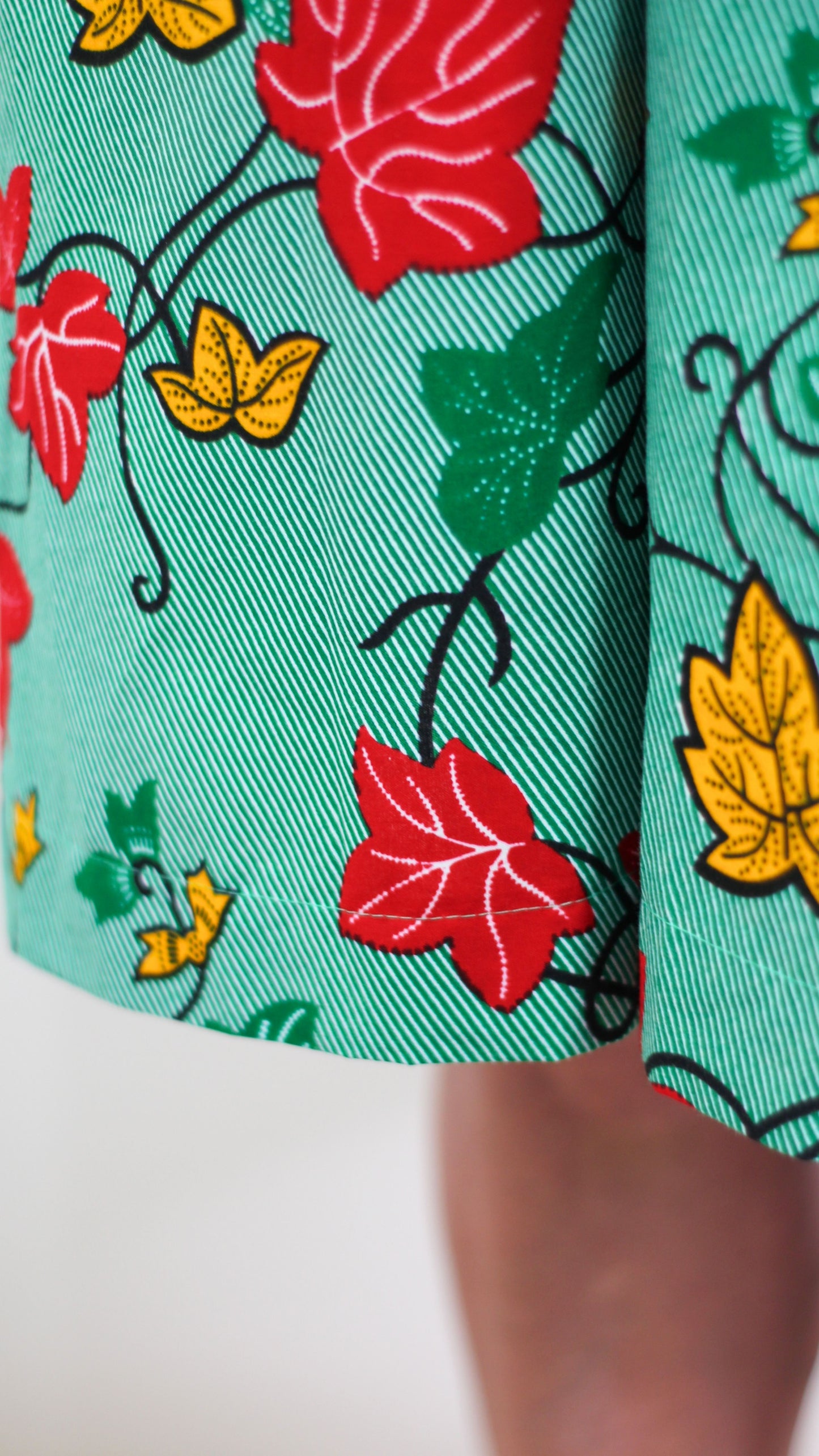 A close up of the red, green and orange leaf design elements of the green fabric print dress.
