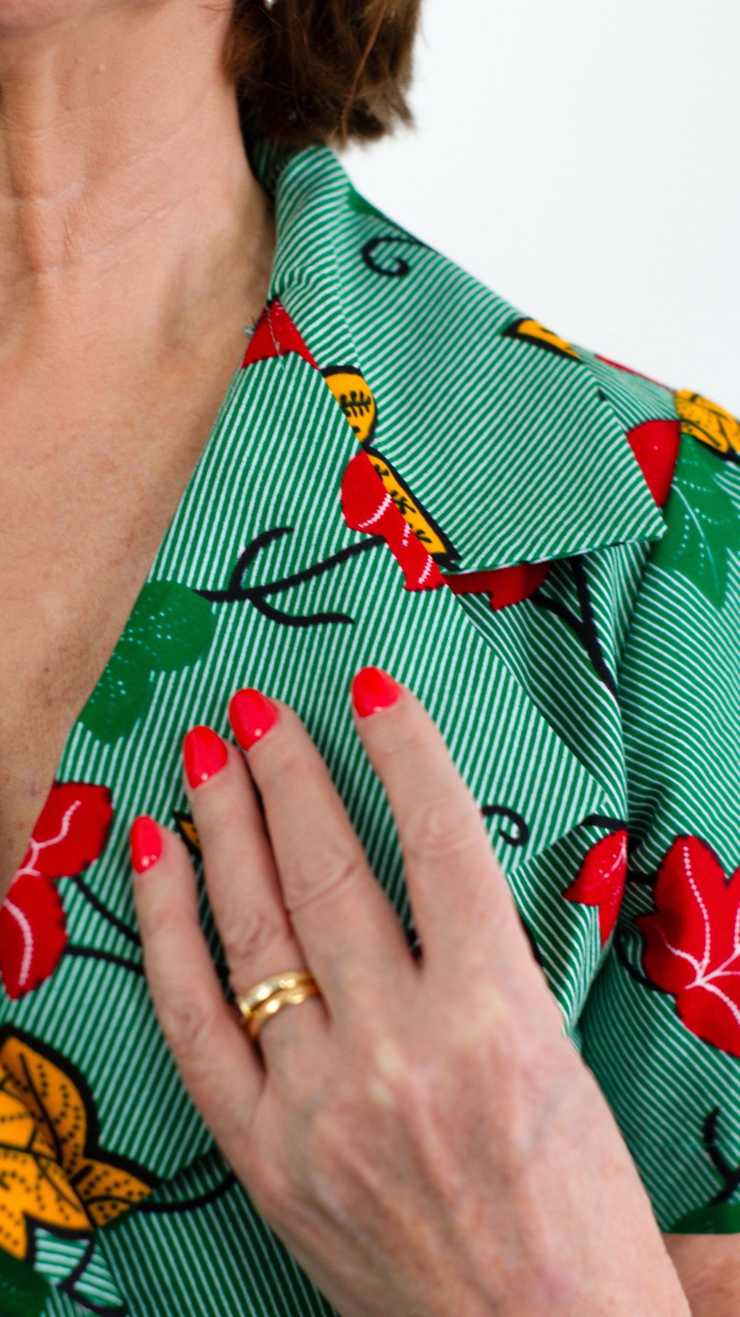 Close view of the neck collar of the green print dress, highlighting the design elements, held by model's hand.