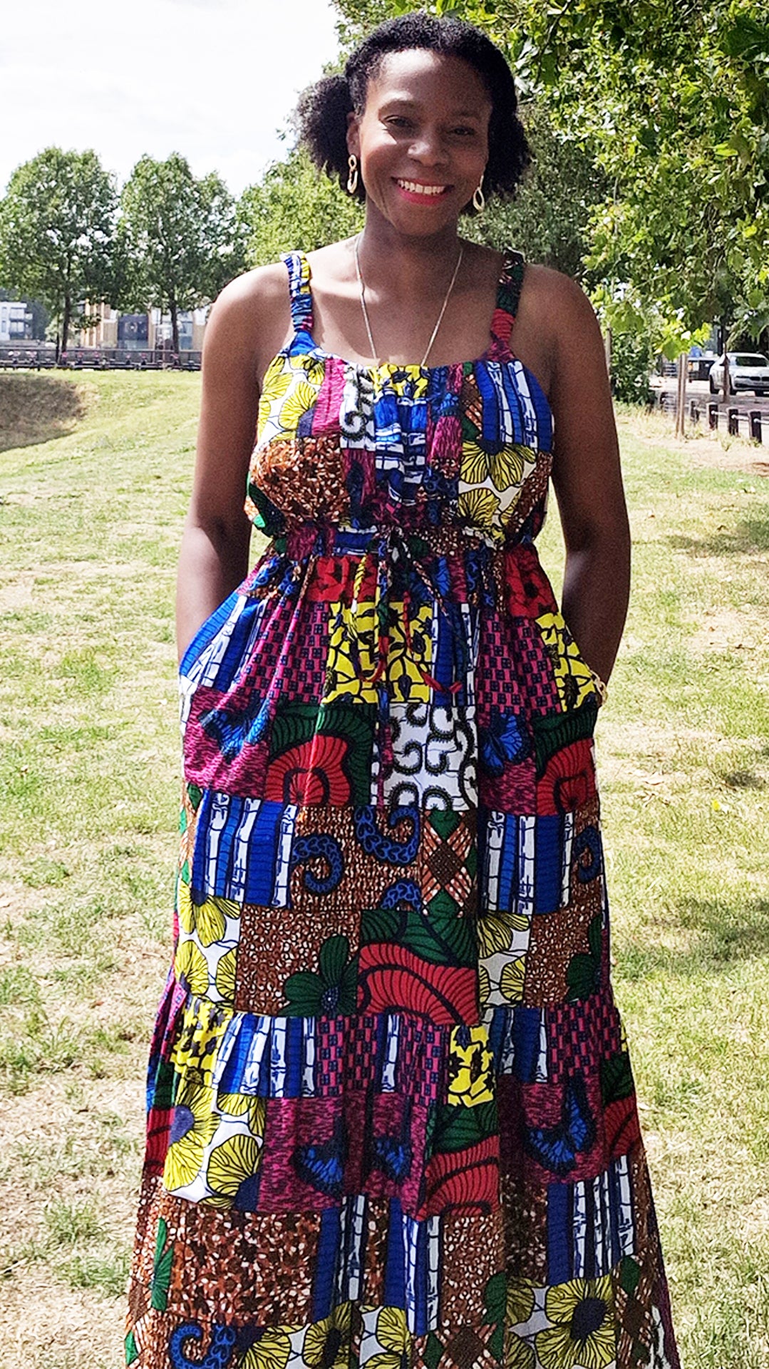 A woman exuding joy and style, gracefully posing with a radiant smile in a maxi long print patchwork dress paired with elegant jewellery in a park setting. 