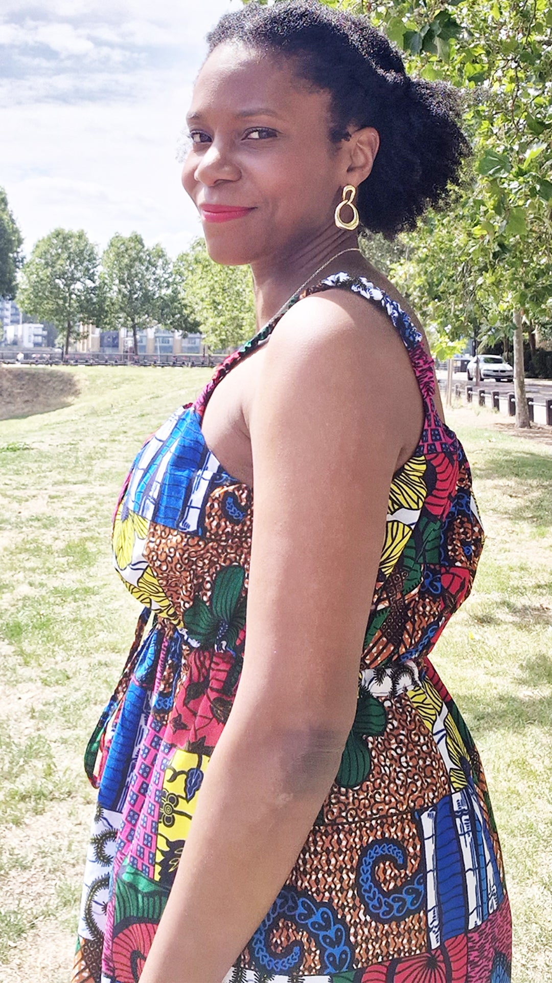 A woman exuding grace, wearing a 3/4 short patchwork dress, the view capturing a shoulder shot in the midst of a picturesque park setting.