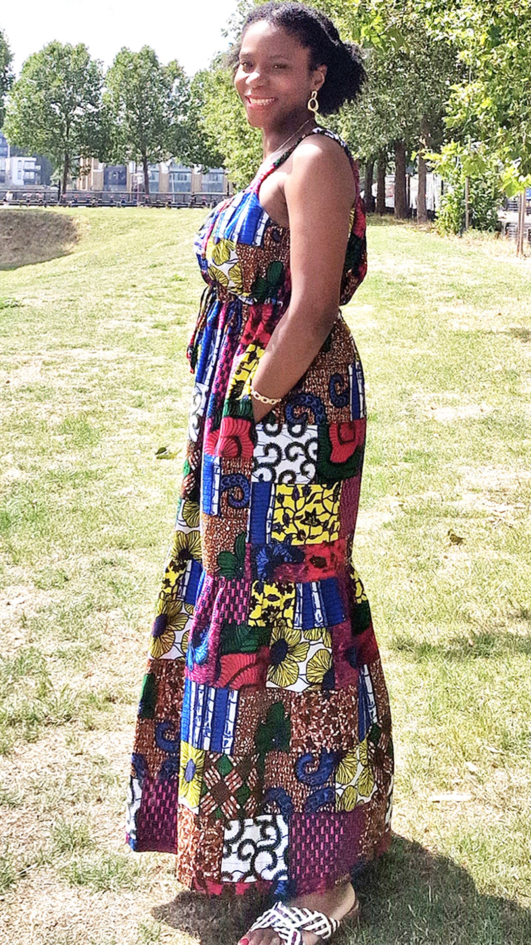 A woman radiates happiness while wearing a maxi print patchwork dress, paired with white sandals.