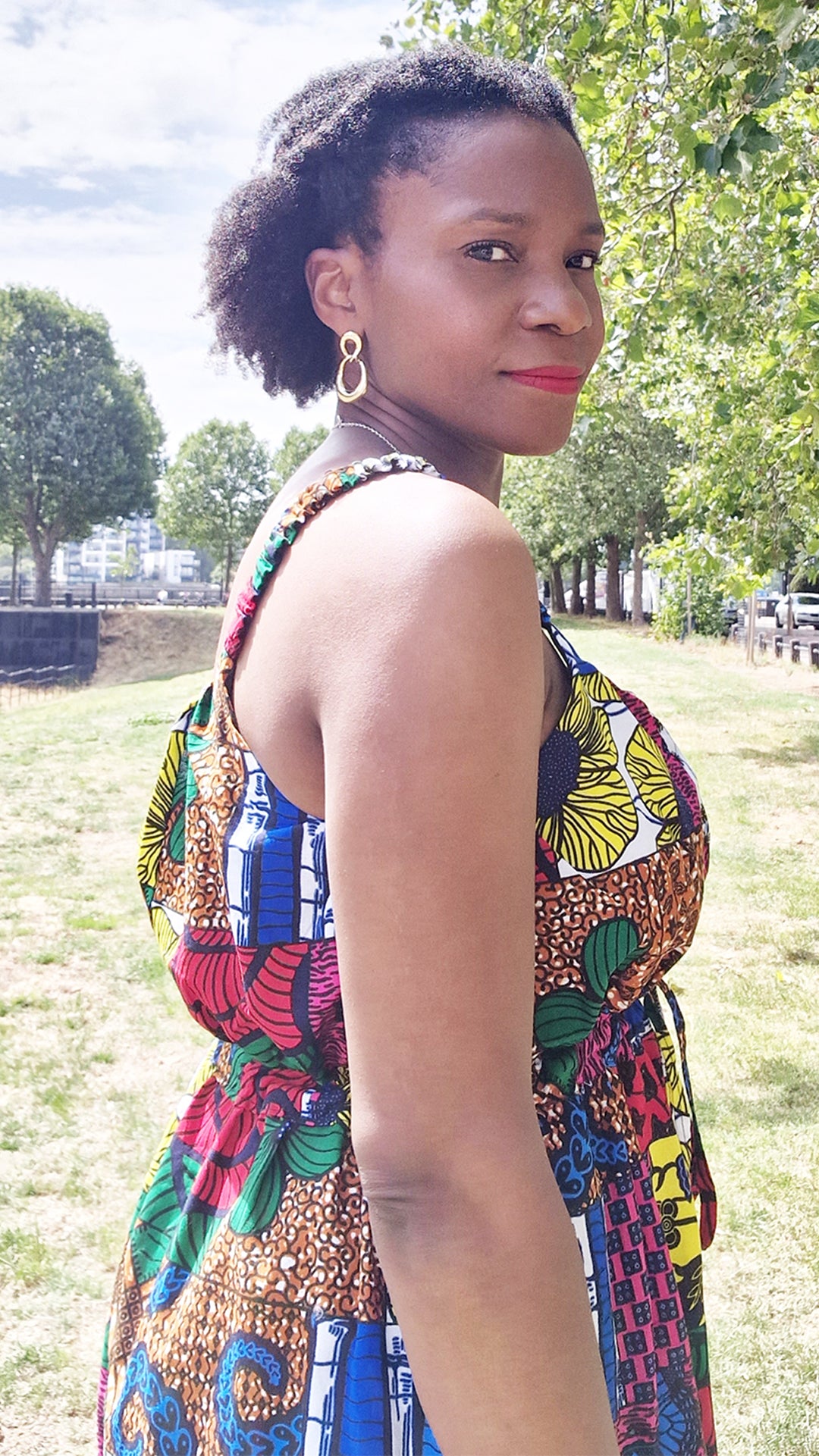 A woman elegantly wearing the 3/4 short patchwork dress, the view capturing a shoulder shot, in a picturesque park setting. The dress stands out against the natural backdrop, showcasing its vibrant colours and stylish elements.