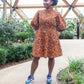 A person exudes happiness in an orange puff-sleeve dress, paired with blue trainers in a garden setting.