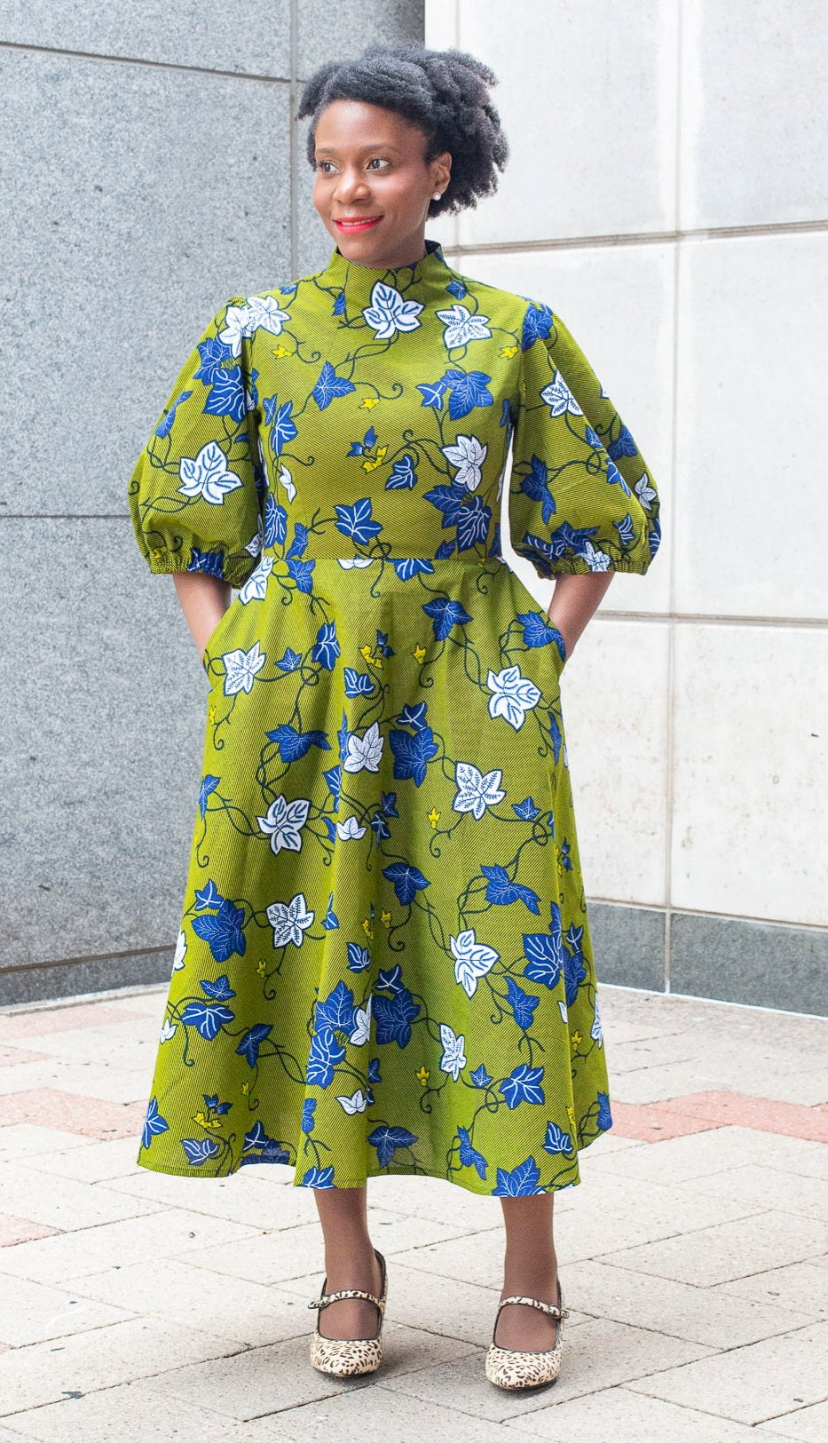 A person exudes happiness in a khaki dress adorned with detailed blue and white leaves, paired with mary janes.