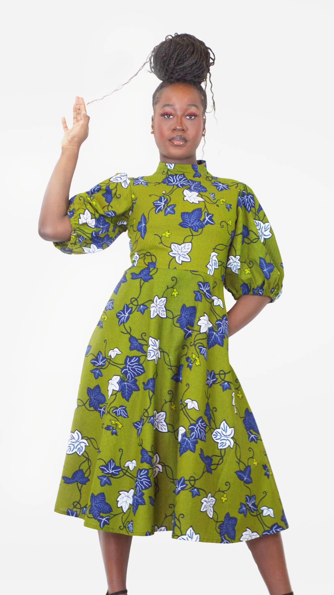 A model confidently poses with arms up, showcasing the intricate blue and white leaf pattern on a khaki long puff sleeve dress. 