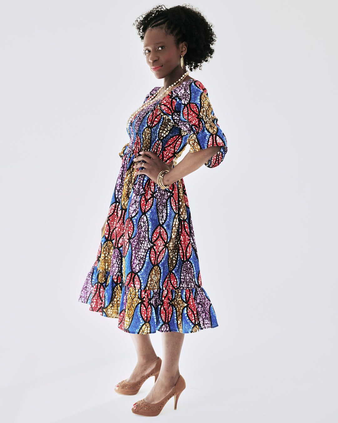 Woman wearing the Amaka Dress, showcasing its vibrant print, smocked bodice, and flared midi skirt.