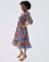 Woman wearing the Amaka Dress, showcasing its vibrant print, smocked bodice, and flared midi skirt.