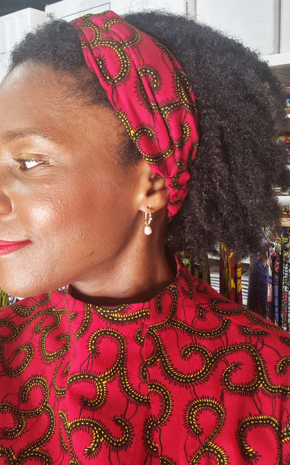 A side profile of a woman wearing the red headband with swirly elements and a matching print dress.