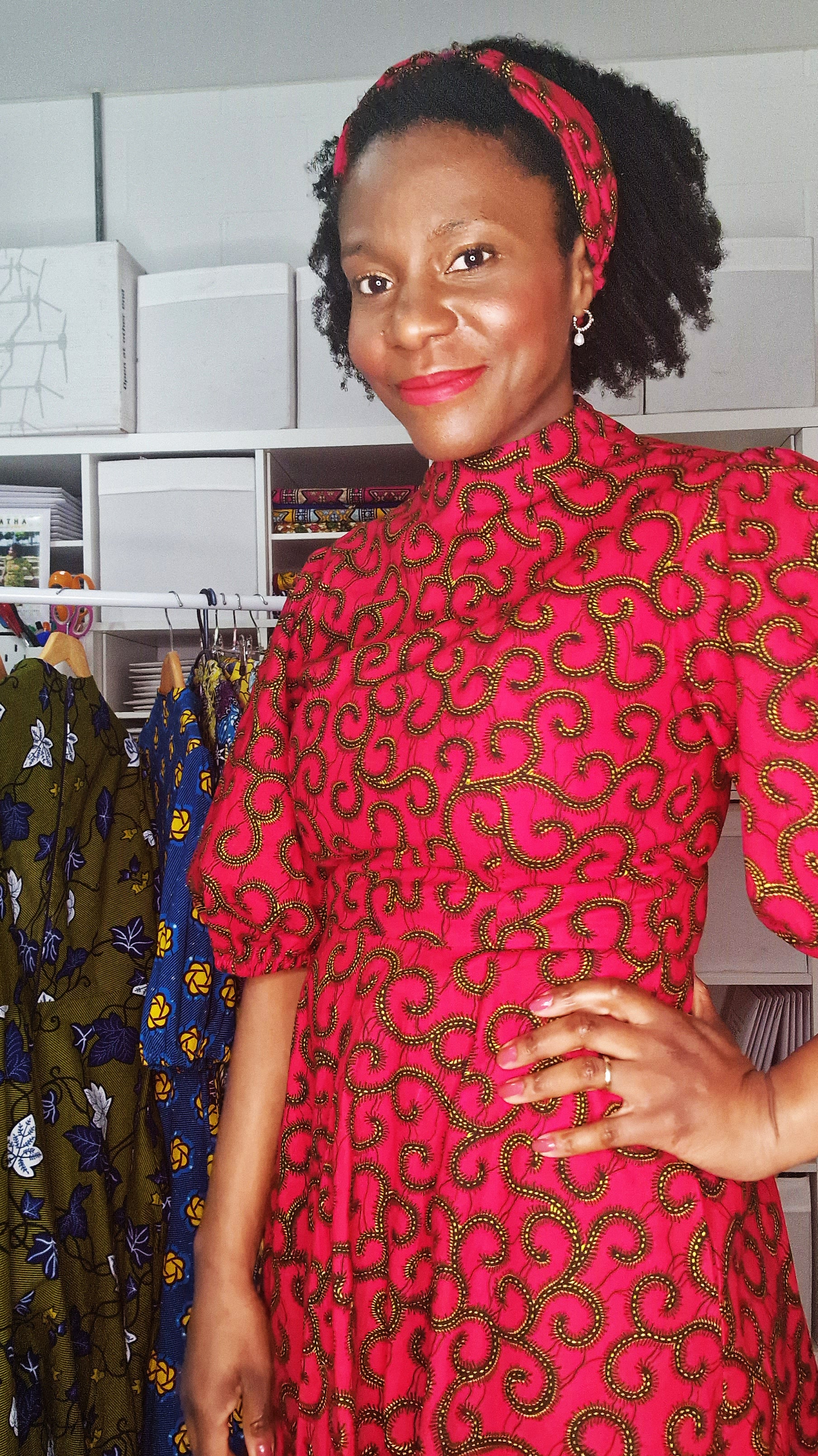 A woman in a room posing with the red headband with swirly elements and a matching print dress.