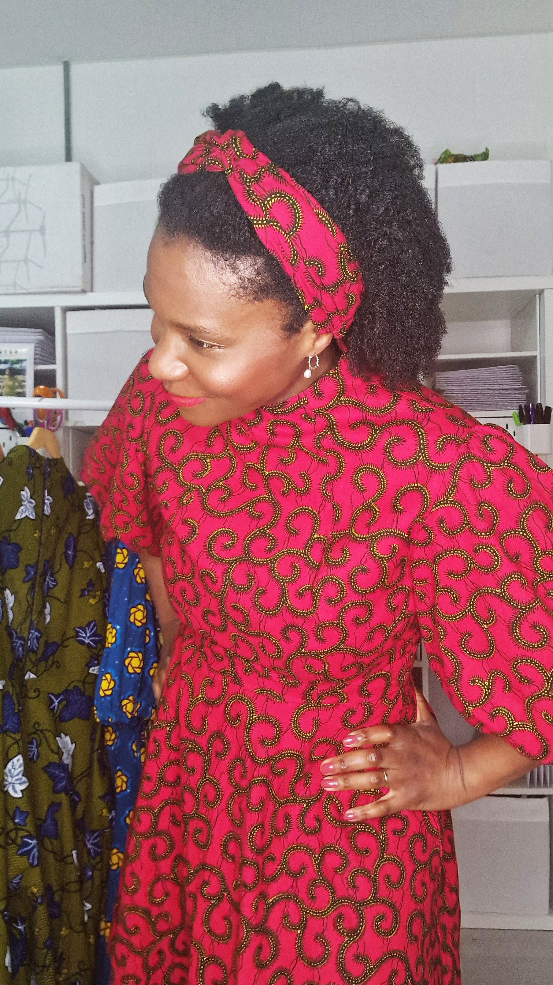 A woman showcasing the red headband with swirly elements and wearing a matching print dress.