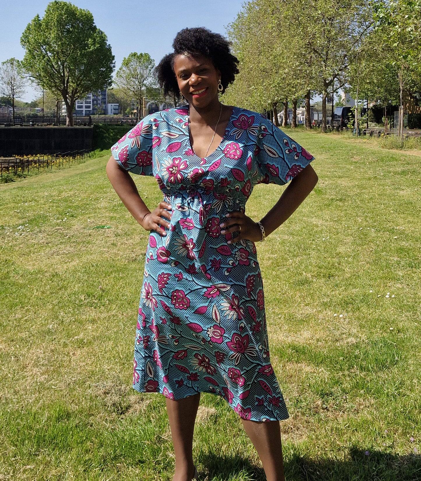 A woman confidently poses confidently wearing a chic blue kaftan dress with a pink floral print. 