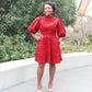 A woman confidently posing in a red puff sleeve dress paired with beige heels.