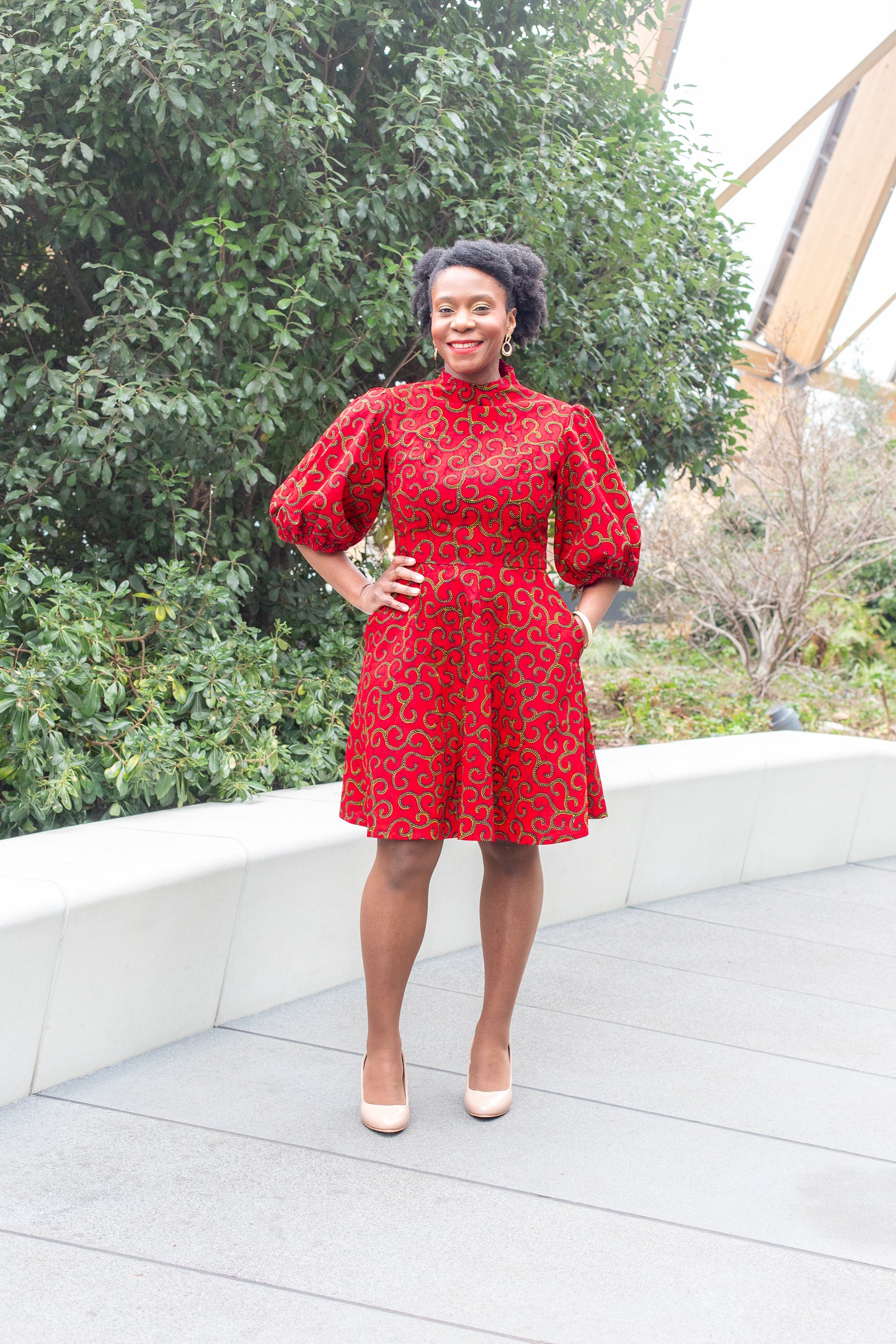 A woman confidently posing in a red puff sleeve dress paired with beige heels.