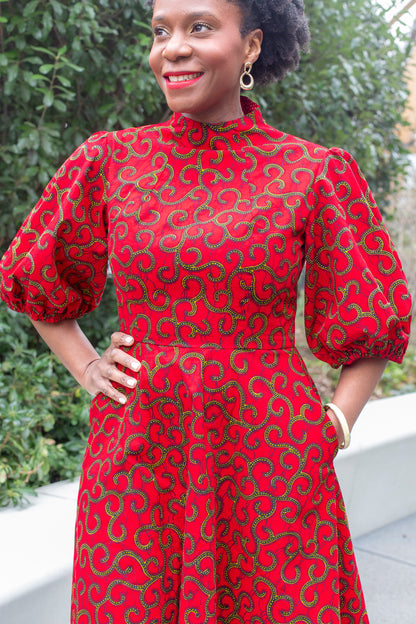 A woman exudes happiness in a red puff-sleeve dress in front of a park setting.