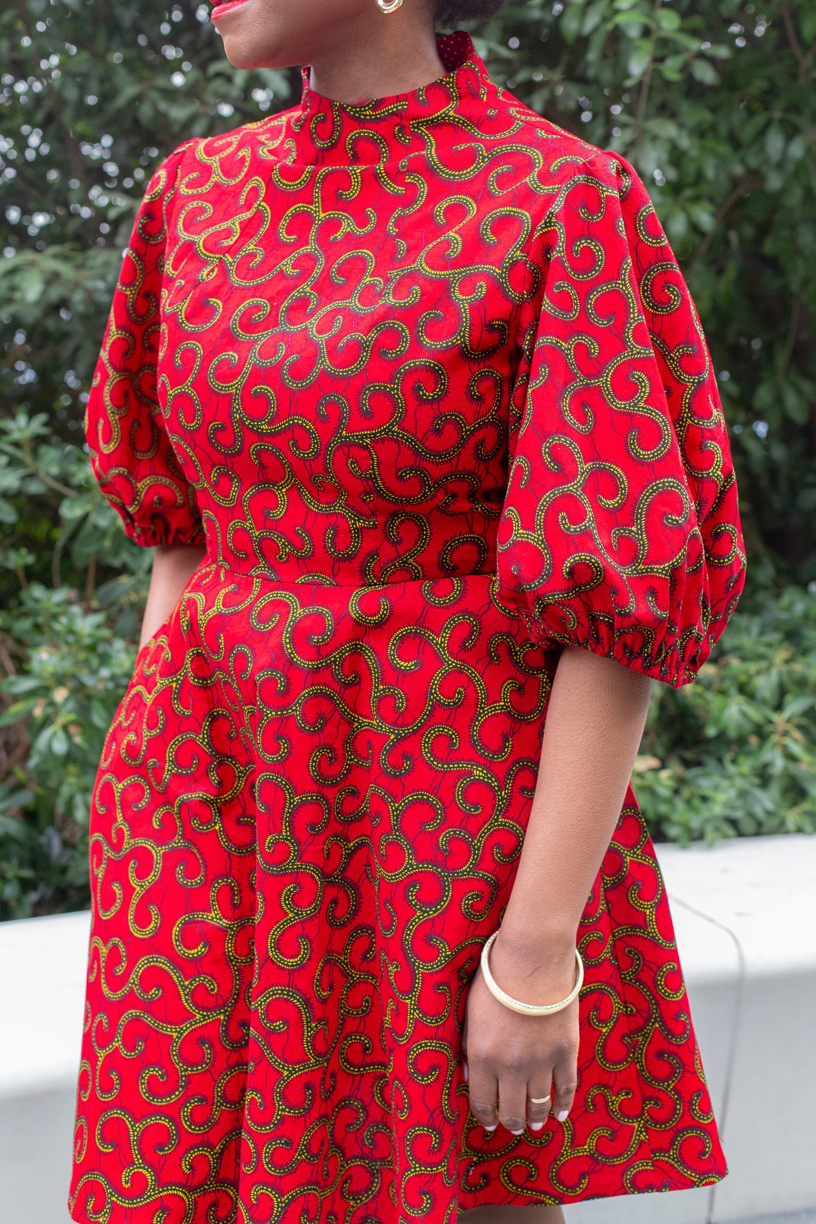 A close up of the swirly golden elements of the red print puff sleeve dress.
