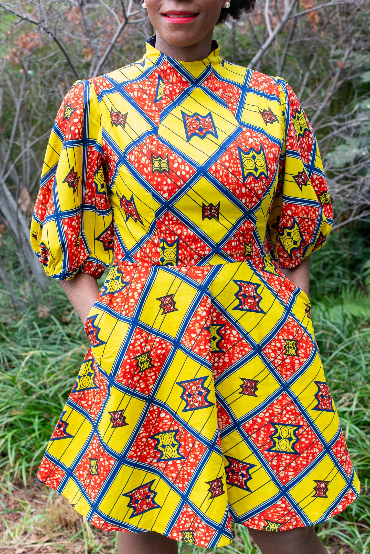 a close up of a woman wearing the short puff sleeve yellow and red print dress, who places hands in her pockets to showcase the comfortability of the dress.